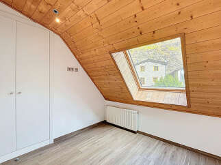 This charming attic room features a unique sloped ceiling with warm wooden paneling, creating a cozy and inviting atmosphere.
