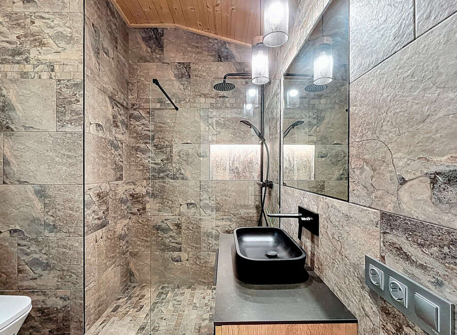 Experience luxury in this stunning bathroom featuring exquisite stone tile work and a sleek black sink.