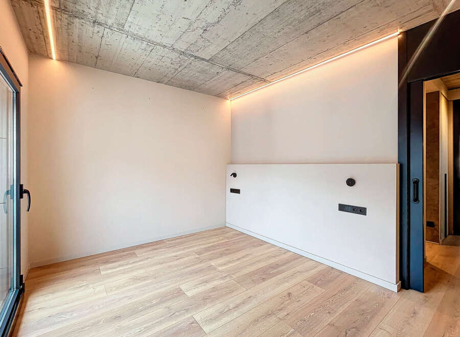 Modern minimalist room with concrete ceiling, LED lighting, and light oak wood flooring.