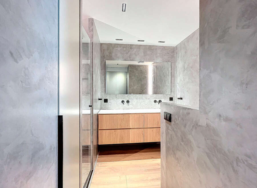 Modern bathroom with double vanity and walk-in shower, featuring sleek light wood cabinets and a minimalist design.