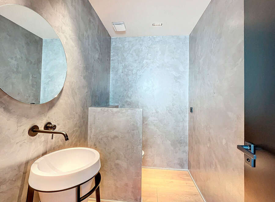 Modern bathroom with concrete walls, a round mirror, and a sleek sink.