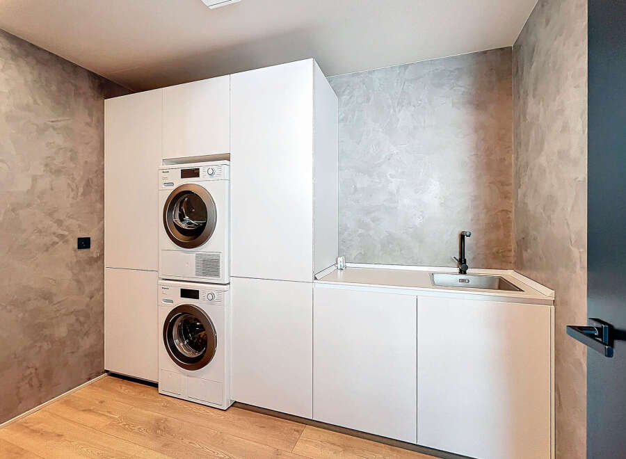 Modern laundry room with built-in washer and dryer, sleek white cabinetry, and a convenient countertop sink.