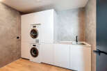 Modern laundry room with built-in washer and dryer, sleek white cabinetry, and a convenient countertop sink.