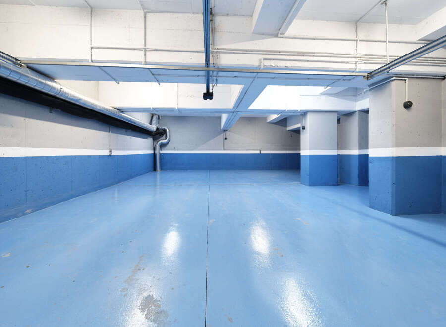 This spacious parking garage boasts a modern design with bright blue epoxy flooring and clean white and gray walls.