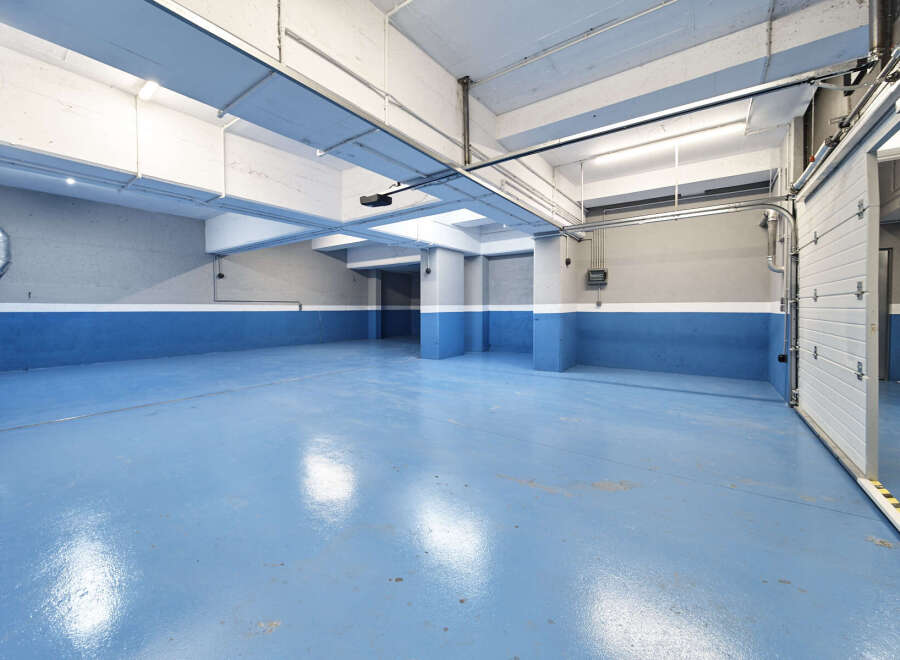This spacious underground parking garage features a sleek, modern design with bright blue epoxy flooring and clean white and gray walls.