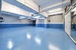 This spacious underground parking garage features a sleek, modern design with bright blue epoxy flooring and clean white and gray walls.