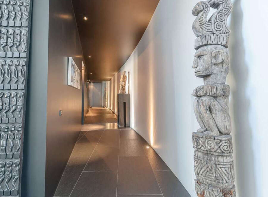 This stunning property boasts a long hallway with dark gray tile flooring, complemented by unique artwork and sculptures.
