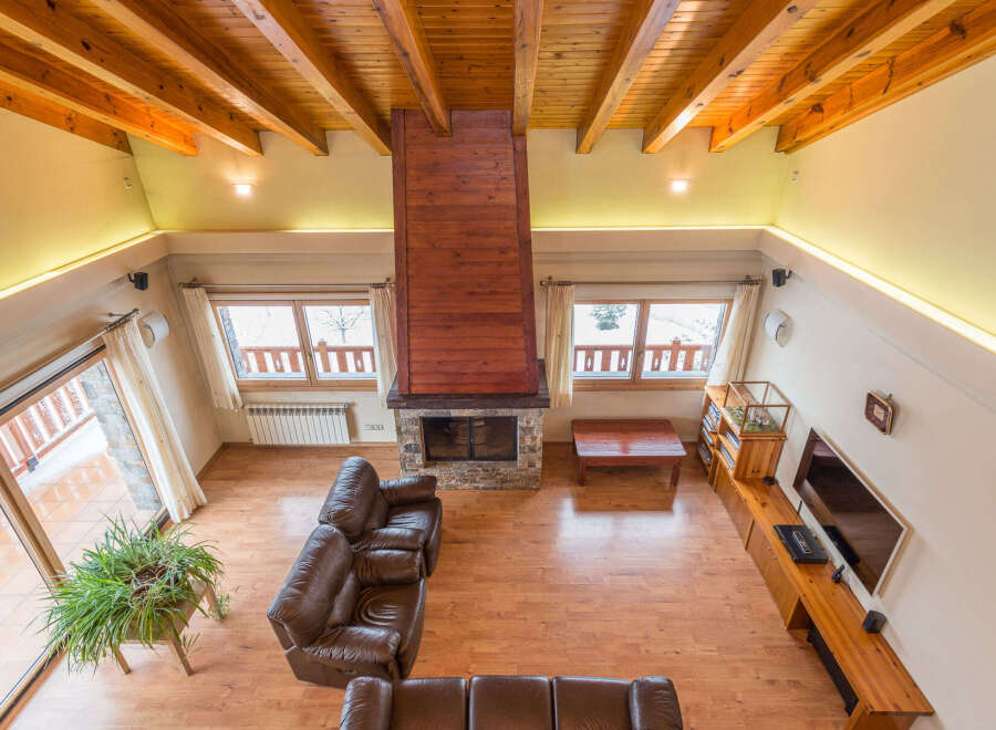 This stunning chalet boasts a spacious open-plan living area with high wooden beamed ceilings and a cozy fireplace as the centerpiece.