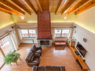 This stunning chalet boasts a spacious open-plan living area with high wooden beamed ceilings and a cozy fireplace as the centerpiece.