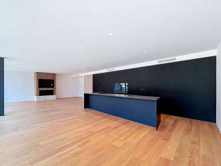 Experience modern living in this spacious open-plan apartment featuring a sleek, dark kitchen island and integrated cabinetry.