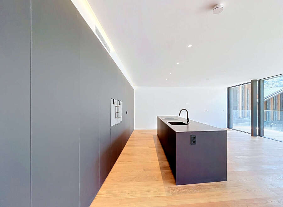 Experience modern living in this sleek, minimalist kitchen featuring a large dark island with a built-in sink and faucet.