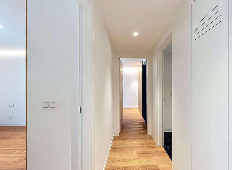 Step into this modern hallway featuring sleek white walls and a warm, inviting wooden floor.