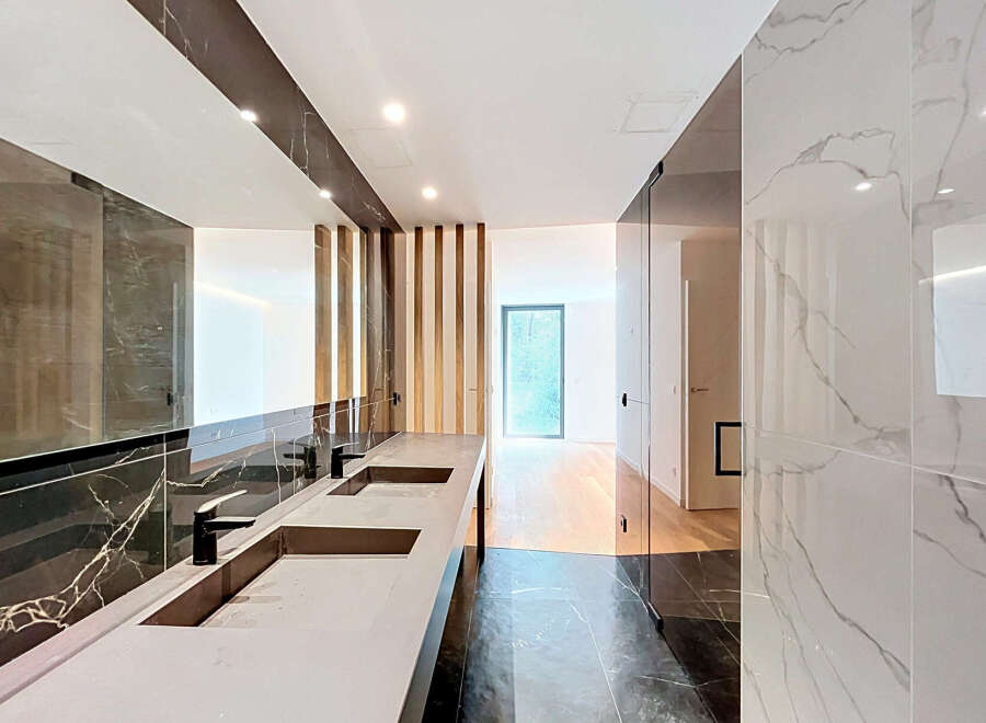 Experience modern luxury in this stunning bathroom featuring a sleek double vanity with contemporary faucets and a large, illuminated mirror.