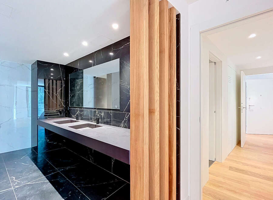 Experience modern luxury in this stunning bathroom featuring a sleek double vanity with integrated sinks and a dramatic black marble accent wall.