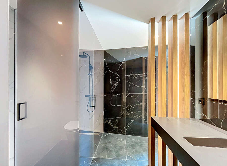 Experience modern luxury in this stunning bathroom featuring a sleek glass-enclosed shower with a rainfall showerhead and a minimalist toilet.
