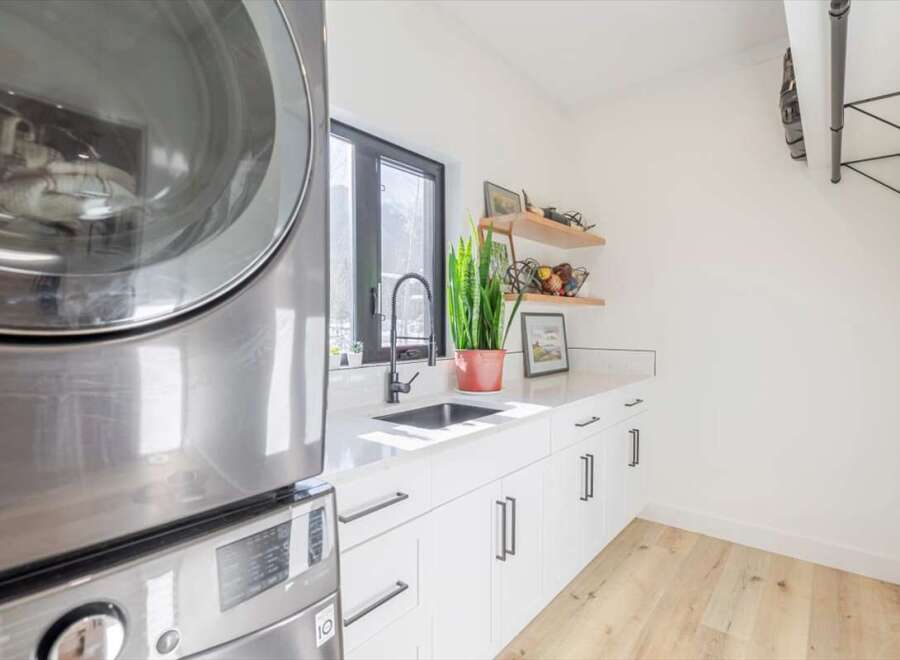 This modern laundry room boasts sleek, white cabinetry and a stylish black faucet.