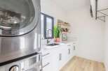This modern laundry room boasts sleek, white cabinetry and a stylish black faucet.