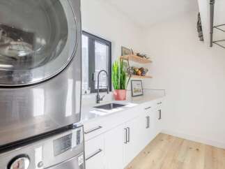 This modern laundry room boasts sleek, white cabinetry and a stylish black faucet.