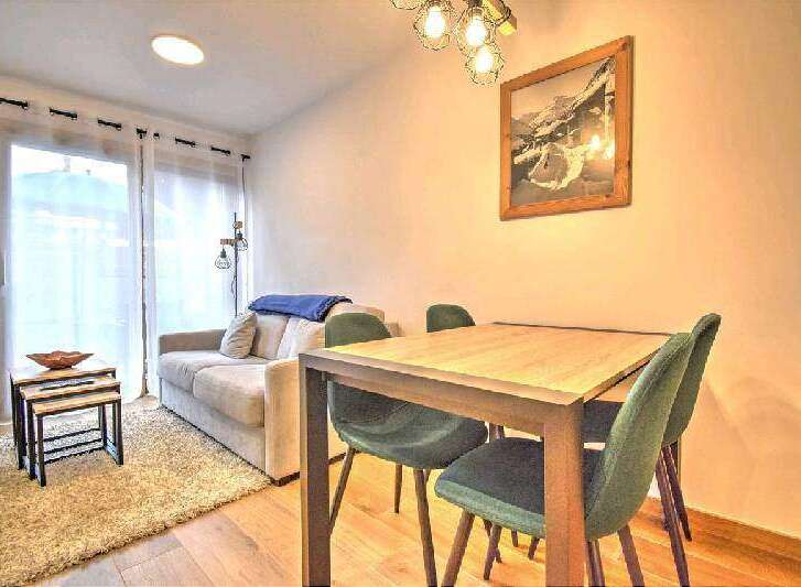 Cozy apartment featuring a comfortable sofa, a dining table with four chairs, and large windows offering plenty of natural light.