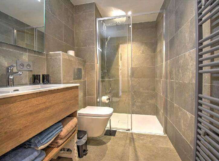 Modern bathroom with sleek wood vanity, spacious shower, and heated towel rack.
