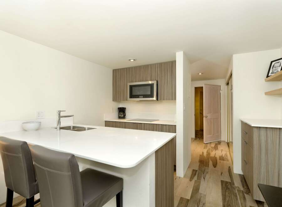 This modern kitchen boasts a sleek white countertop island with two brown leather barstools, perfect for casual dining.