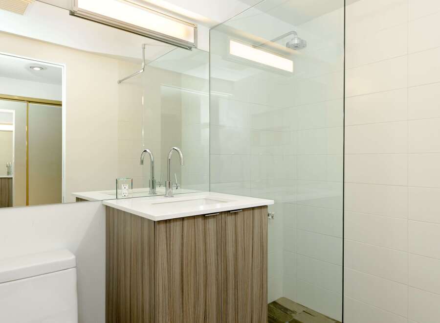 This modern bathroom boasts a sleek glass shower enclosure, contemporary wood-look vanity, and stylish chrome fixtures.