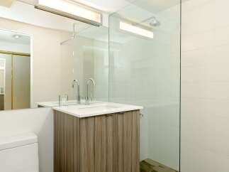 This modern bathroom boasts a sleek glass shower enclosure, contemporary wood-look vanity, and stylish chrome fixtures.