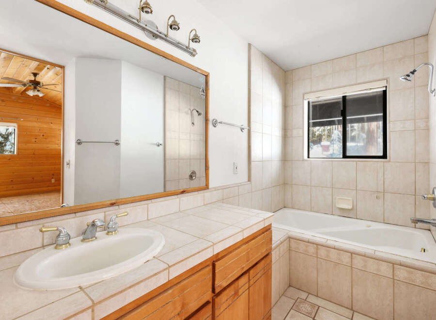 This charming bathroom boasts a wood vanity, complementing the wood-paneled adjacent room visible through the mirror.