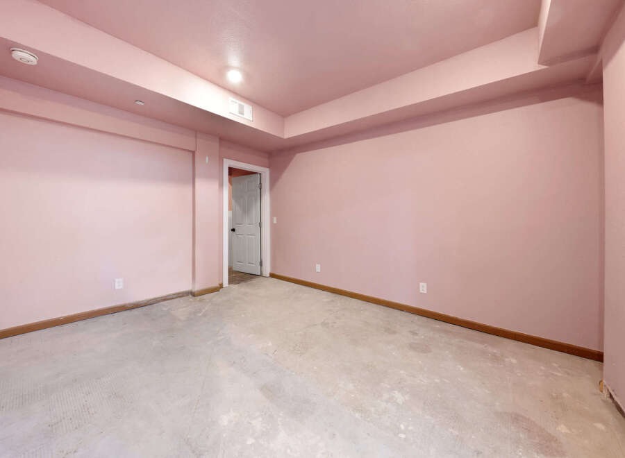 This spacious room features light pink walls and a concrete floor, offering a blank canvas for customization.