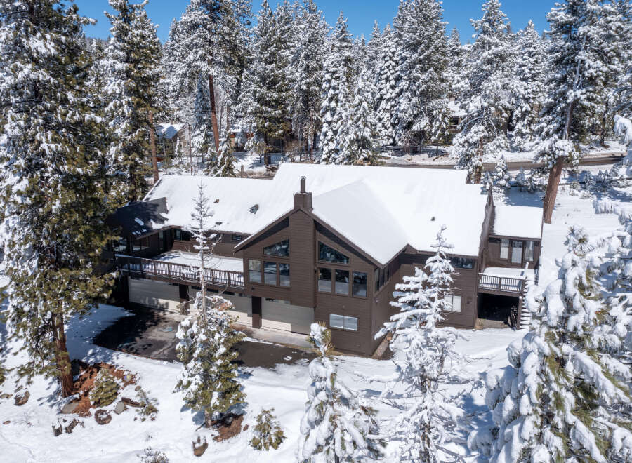 This stunning mountain home boasts a spacious layout with multiple levels, large windows offering breathtaking views, and a sizable deck perfect for enjoying the snowy landscape.