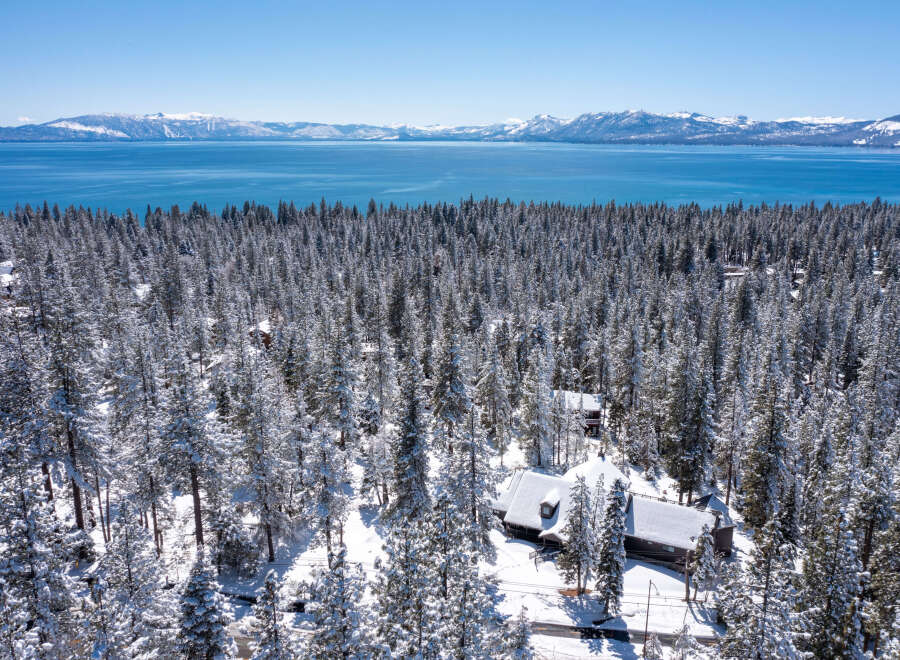 This stunning property boasts a spacious, snow-covered cabin nestled amongst a breathtaking snowy forest, offering unparalleled views of a crystal-clear lake and majestic mountains in the distance.