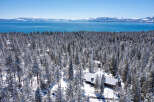 This stunning property boasts a spacious, snow-covered cabin nestled amongst a breathtaking snowy forest, offering unparalleled views of a crystal-clear lake and majestic mountains in the distance.