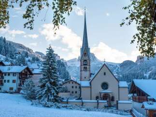 Nestled in a snow-covered mountain village, this charming church boasts a tall, pointed spire and a tranquil atmosphere.