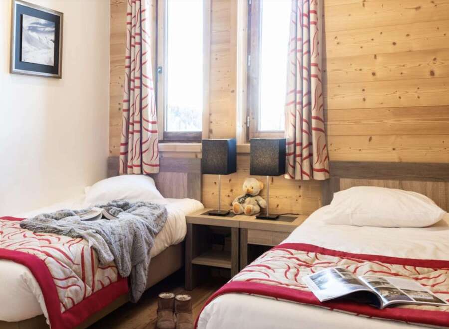 Cozy twin bedroom with wood-paneled walls and red and cream patterned bedspreads.