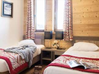 Cozy twin bedroom with wood-paneled walls and red and cream patterned bedspreads.