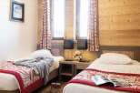 Cozy twin bedroom with wood-paneled walls and red and cream patterned bedspreads.