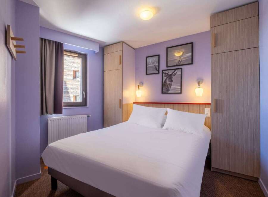 This cozy hotel room features a comfortable double bed, ample closet space, and tasteful wall art.