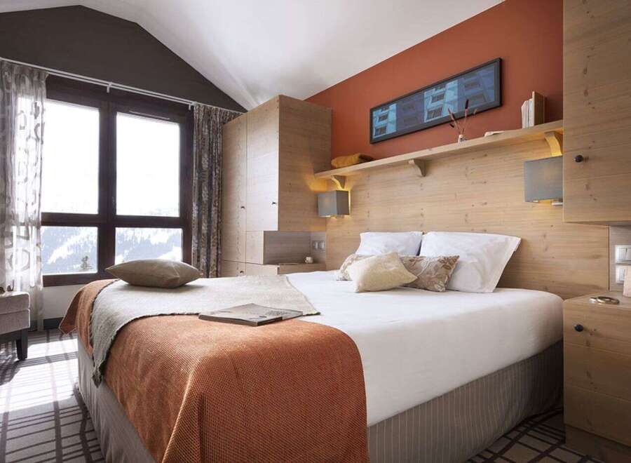 Cozy bedroom with a wooden headboard and built-in wardrobe, offering stunning mountain views from large windows.