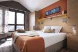 Cozy bedroom with a wooden headboard and built-in wardrobe, offering stunning mountain views from large windows.