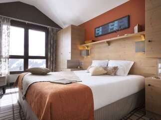 Cozy bedroom with a wooden headboard and built-in wardrobe, offering stunning mountain views from large windows.