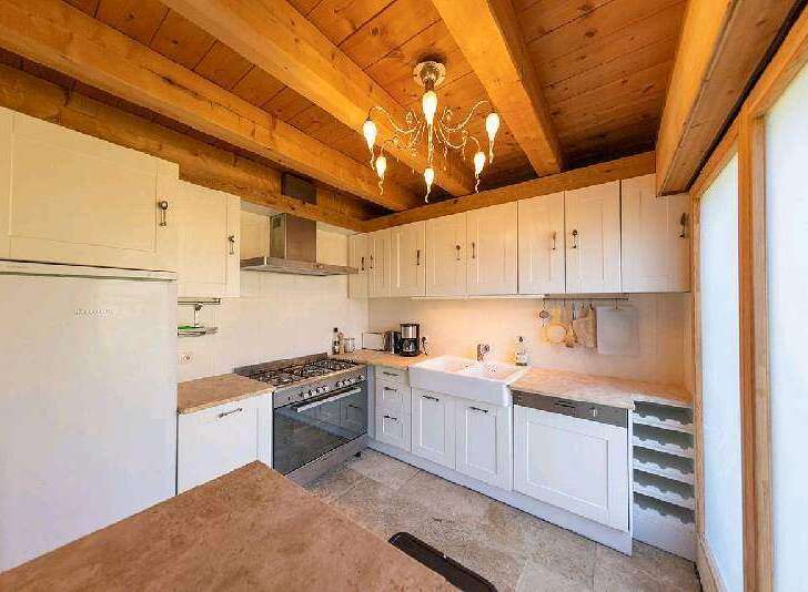 This stunning kitchen boasts a charming wooden beam ceiling and a beautiful chandelier, creating a warm and inviting atmosphere.
