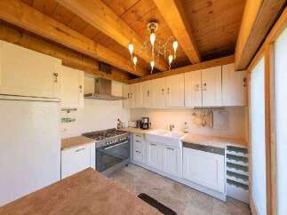 This stunning kitchen boasts a charming wooden beam ceiling and a beautiful chandelier, creating a warm and inviting atmosphere.