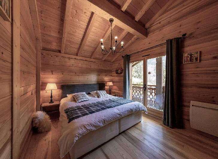 Cozy chalet bedroom with wooden walls and ceilings, featuring a comfortable double bed and a view of the snowy mountains.