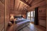 Cozy chalet bedroom with wooden walls and ceilings, featuring a comfortable double bed and a view of the snowy mountains.