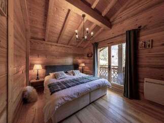 Cozy chalet bedroom with wooden walls and ceilings, featuring a comfortable double bed and a view of the snowy mountains.