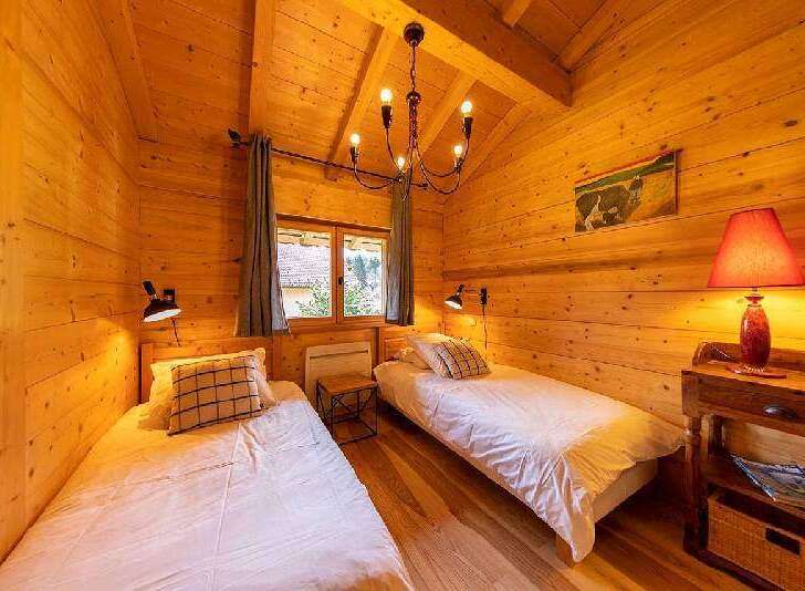 Cozy chalet bedroom with twin beds, wooden walls, and a rustic chandelier.
