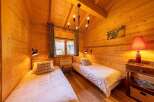 Cozy chalet bedroom with twin beds, wooden walls, and a rustic chandelier.