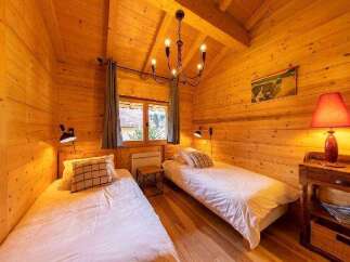 Cozy chalet bedroom with twin beds, wooden walls, and a rustic chandelier.