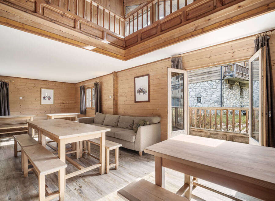 This stunning chalet boasts a spacious open-plan living area with multiple wooden dining tables perfect for large groups.