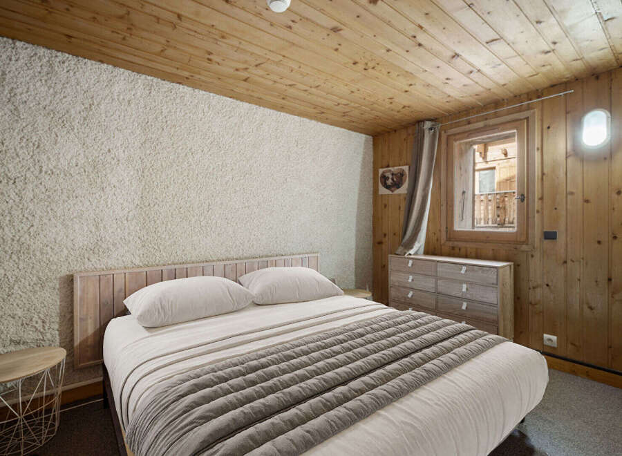 Cozy chalet bedroom with wooden walls and ceiling, featuring a comfortable double bed and a rustic dresser.